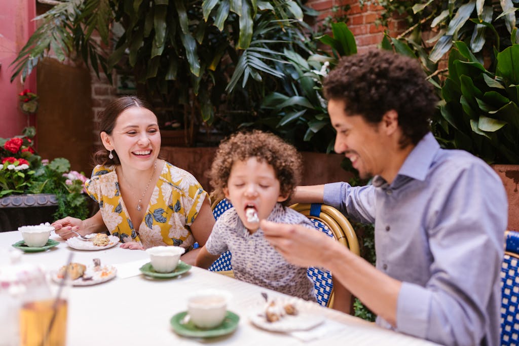 Happy family sharing dessert together at an outdoor cafe with lush greenery.